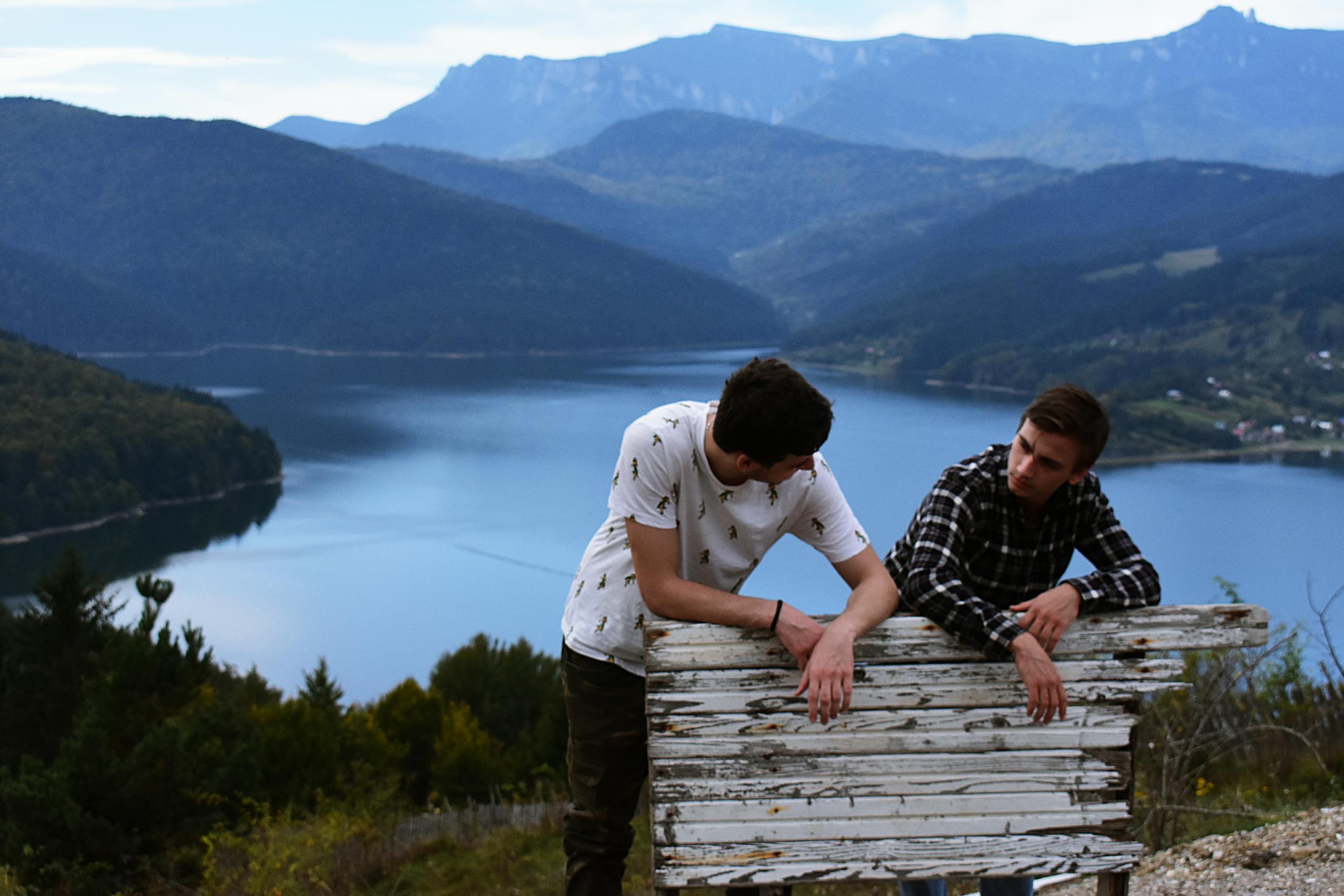Two young men enjoy a scenic view of a mountain lake, surrounded by nature.